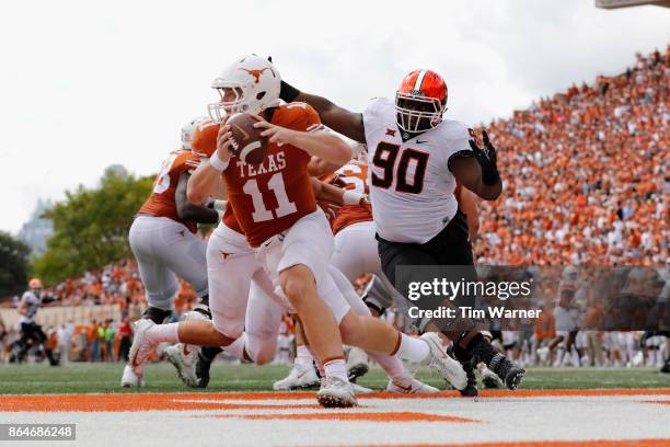 Sam Ehlinger of the Texas Longhorns is forced to scramble under pressure by Taaj Bakari of the Oklahoma State Cowboys in the second quarter at...