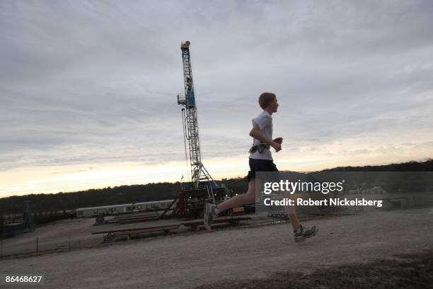 Jogger runs past a 150-foot derrick positioned over a natural gas well site along a trail at a Trinity River embankment on December 19, 2008 in Fort...