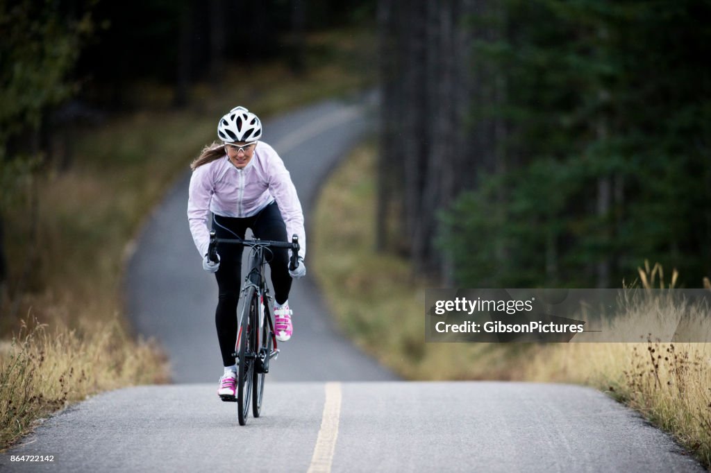 Uma mulher monta sua bicicleta de estrada ao longo do bikepath de Trans Canadá trilha perto de Canmore, Alberta, Canadá no outono.