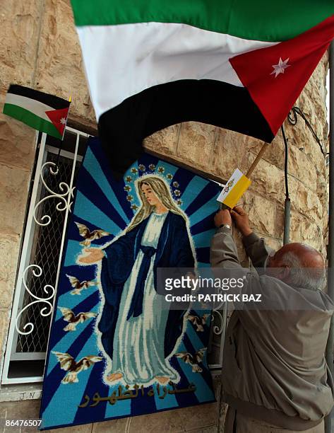 Jordanian Christian man hangs his national flag and the Vatican's flag next to a picture of the Virgin Mary in the southern city of Madaba on May 7,...