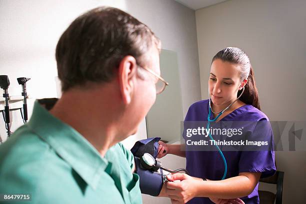 nurse taking patients blood pressure - asistant stock-fotos und bilder