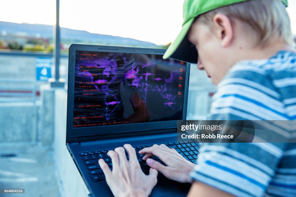 A teenage boy hacking with a laptop computer to commit cyber crime