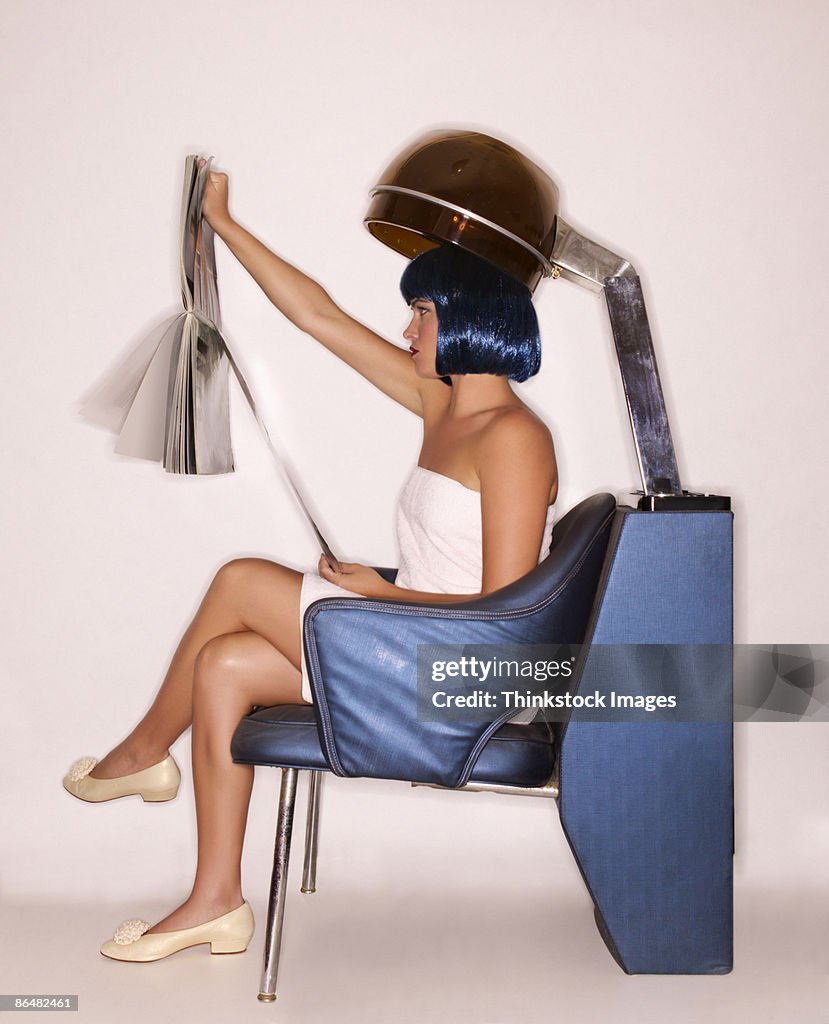 Woman under hairdryer reading magazine