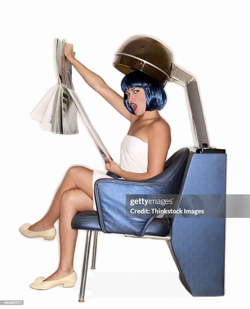 Woman reading magazine under salon hair dryer