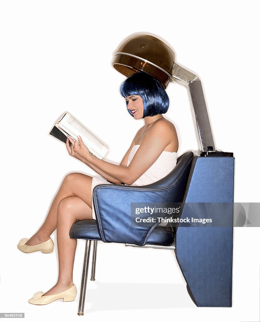 Woman reading magazine under salon hair dryer