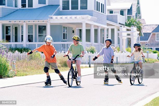 children riding bicycles and inline skating down street - kniebeschermer stockfoto's en -beelden