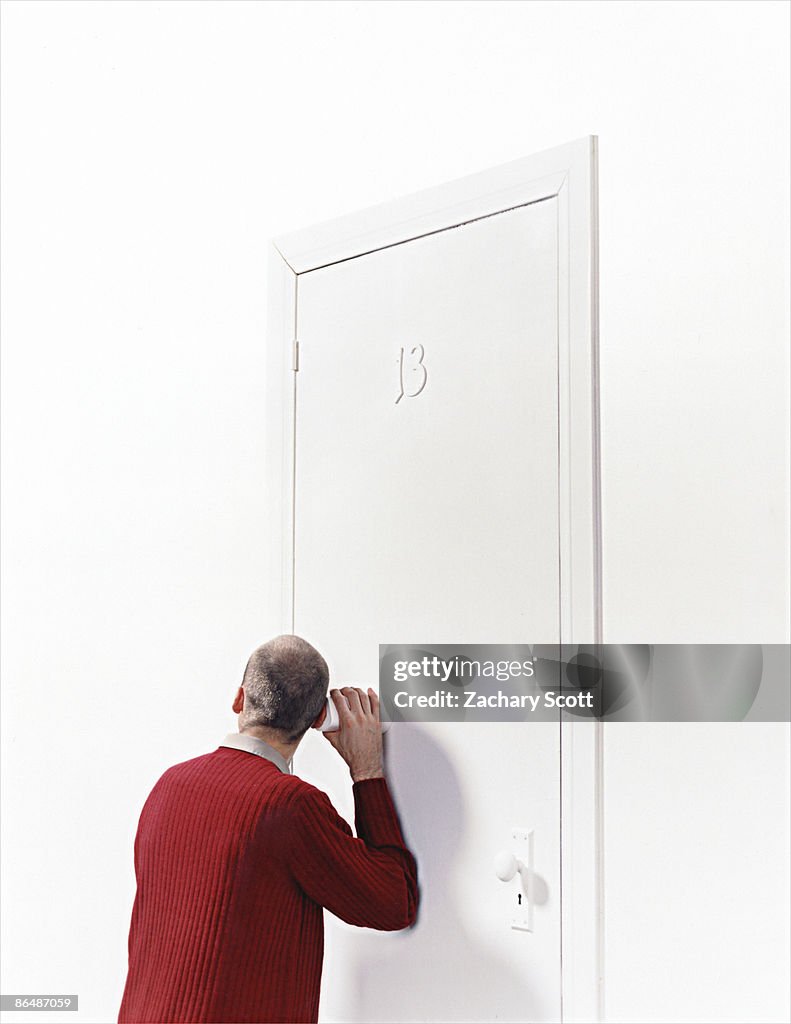 Man listens to a door with a cup