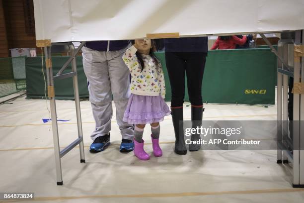 Japanese girl looks at her parents as they fill in their ballot papers at a polling station to vote in Japan's general election in Tokyo on october...