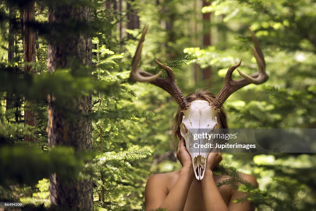 Woman using deer skull as mask in woods