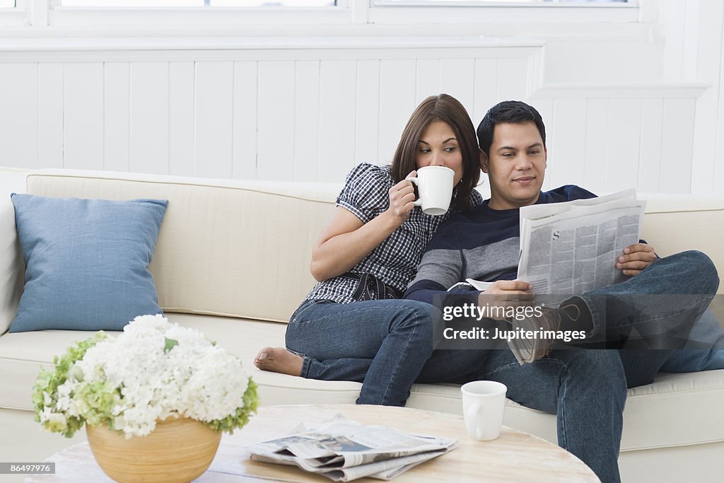 Couple drinking from coffee mugs and reading newspaper