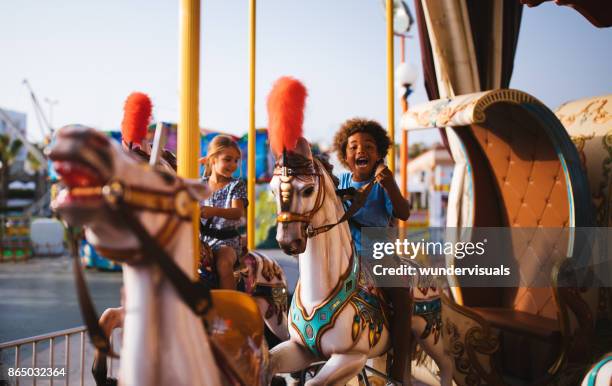 multi-ethnischen kinder spaß am kirmes karussell karussell fahren - freizeitpark stock-fotos und bilder