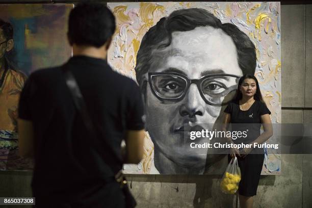 People gather to pay their respects next to a painting of Thailand's late King Bhumibol Adulyadej as the city prepares for his cremation on October...