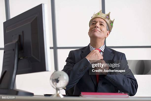 businessman with crown sitting at desk - arrogancia fotografías e imágenes de stock