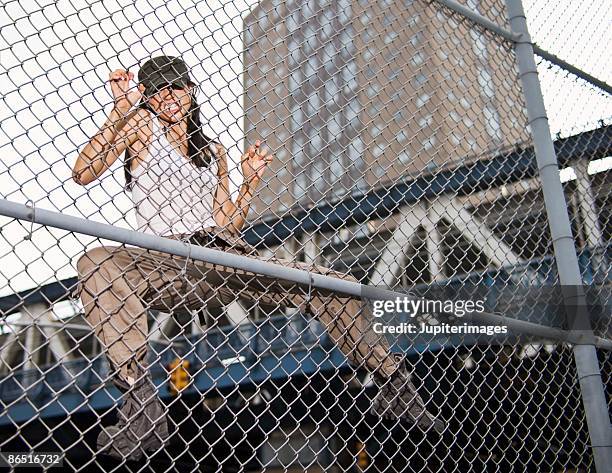 woman climbing chain link fence - chain link fence stock-fotos und bilder