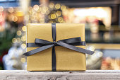 Golden wrapped gift box with black ribbon on a wooden table isolated on golden boked background