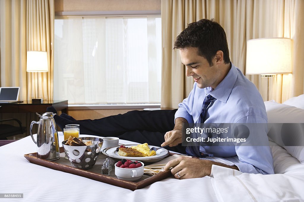 Businessman eating breakfast in bed in hotel room