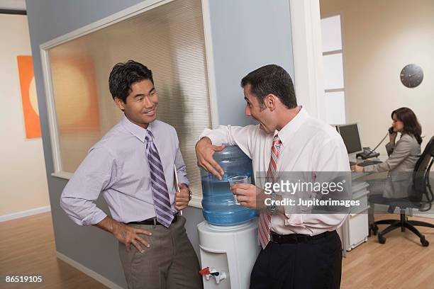 men standing at water cooler in office - dispensador de agua fotografías e imágenes de stock