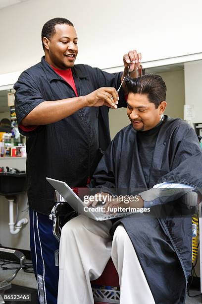 man using laptop while getting haircut - busy barber shop stock pictures, royalty-free photos & images