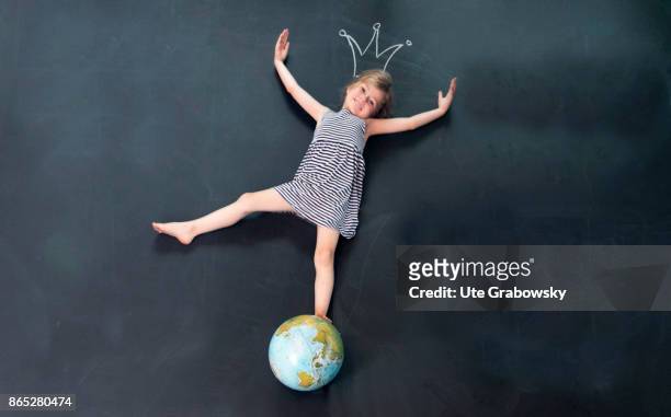 Girl balances on a globe in front of a blackboard. Above her head a crown is painted with chalk on the blackboard on August 08, 2017 in Sankt...