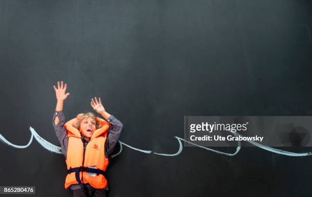 Sankt Augustin, Germany A boy with rescue vest swims in front of a blackboard in an illustrated sea and threatens to sink on August 08, 2017 in Sankt...