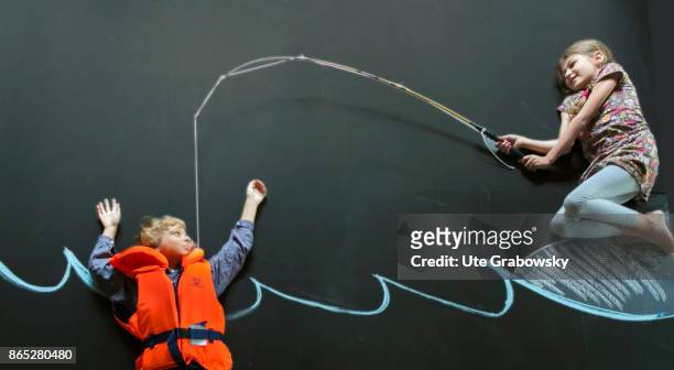Boy with rescue vest swims in front of a blackboard in an illustrated sea and threatens to sink. A girl saves him with a fishing rod on August 08,...