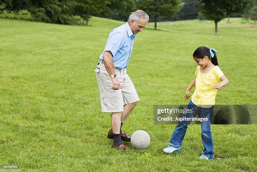 Grandfather and granddaughter kicking soccer ball around