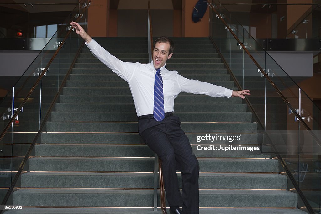 Businessman sliding down banister