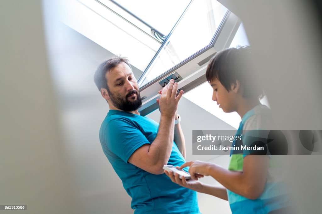 Father and son together checking roof window in smart house