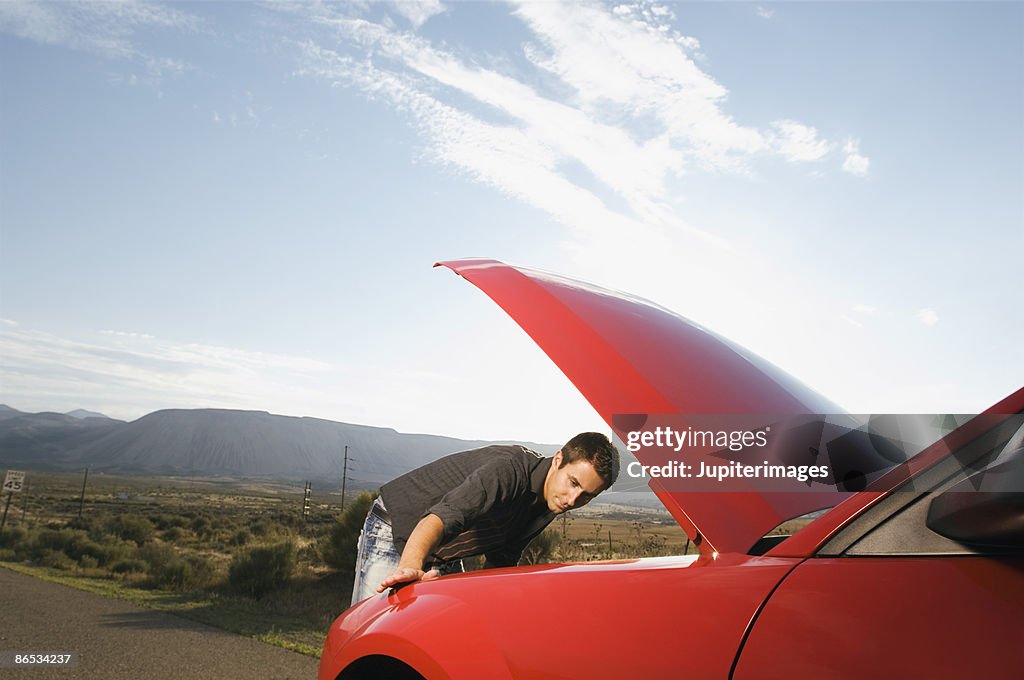 Man looking at car engine at side of road