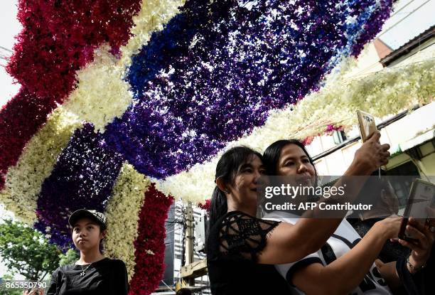 Women take photographs with a Thai flag made of flowers in honour of the late Thai king Bhumibol Adulyadej at Pak Khlong Talad flower market in...