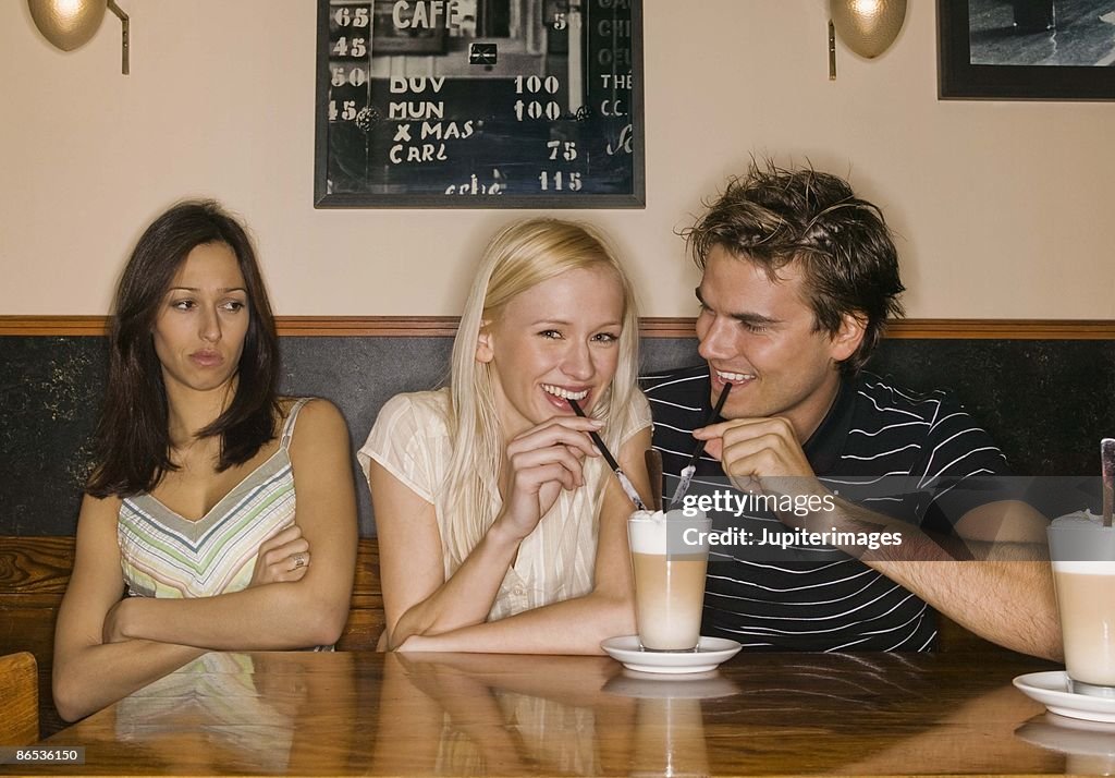 Jealous woman with couple sharing coffee