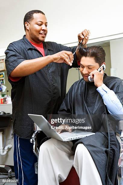 man getting haircut at barbershop using cell phone and laptop - busy barber shop stock pictures, royalty-free photos & images