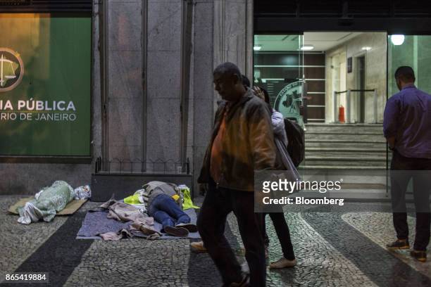 Pedestrians pass in front of people sleeping on a street outside the Public Defender headquarters in Rio de Janeiro, Brazil, on Thursday, Aug. 24,...