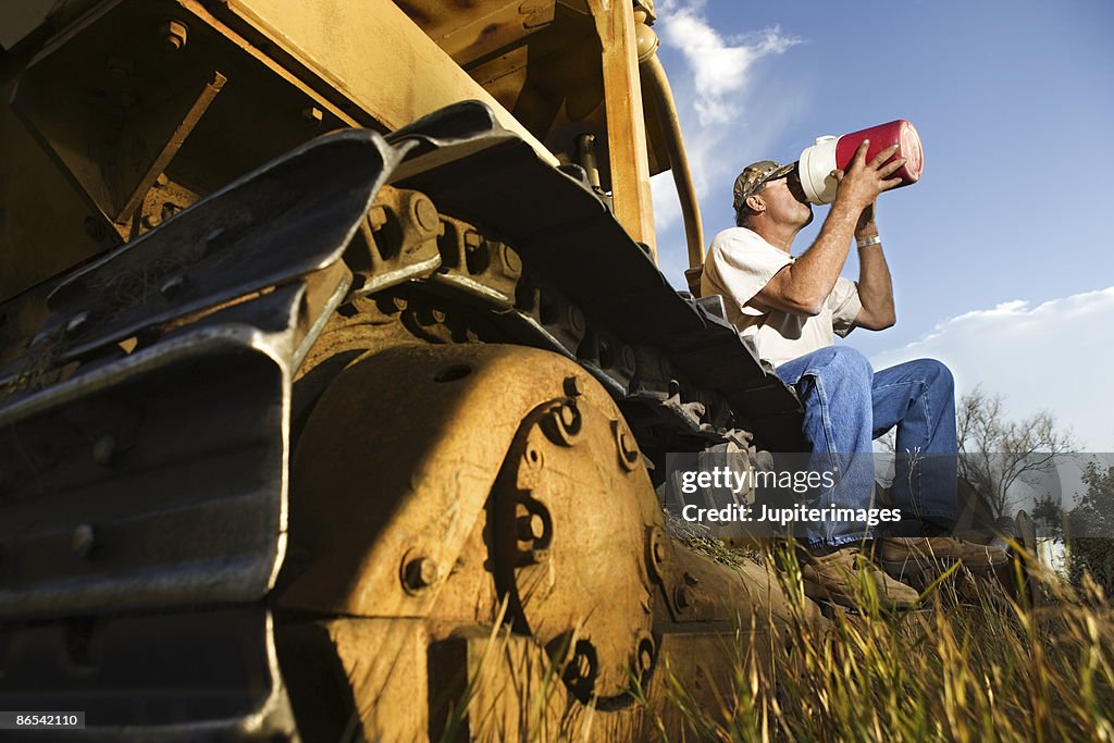 Man sitting on bulldozer drinking from jug