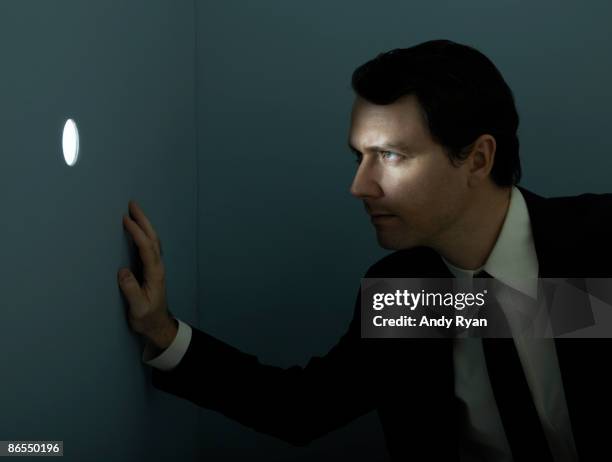 businessman peering through illuminated peep hole. - looking through hole stock pictures, royalty-free photos & images