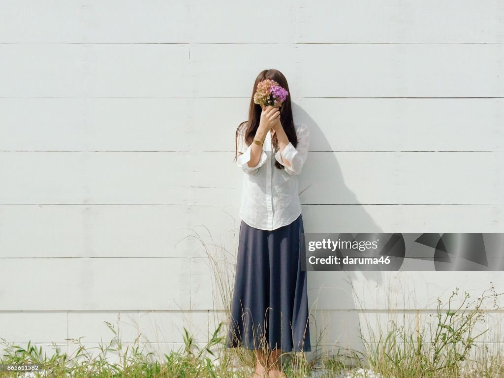 Woman Standing by Wall Covering Face with Flowers