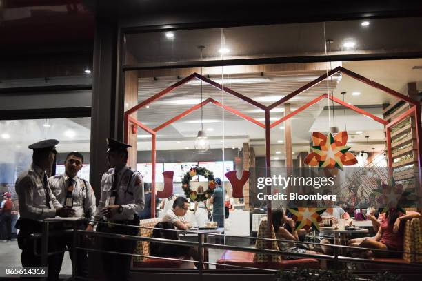 Security guards stand outside as customers dine at a Jollibee Foods Corp. Restaurant in the Bonifacio Global City triangle area of Manila, the...