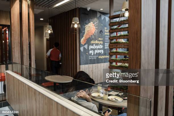 Customers use a smart phone while dining at a Jollibee Foods Corp. Restaurant in the Bonifacio Global City triangle area of Manila, the Philippines,...