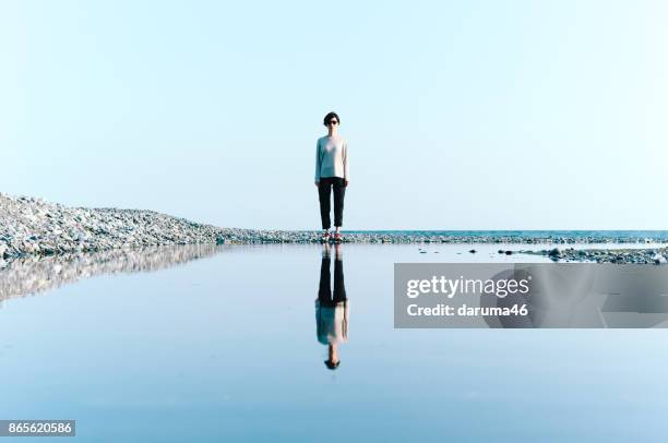 woman standing by beach reflected in big puddle - water reflection stock pictures, royalty-free photos & images