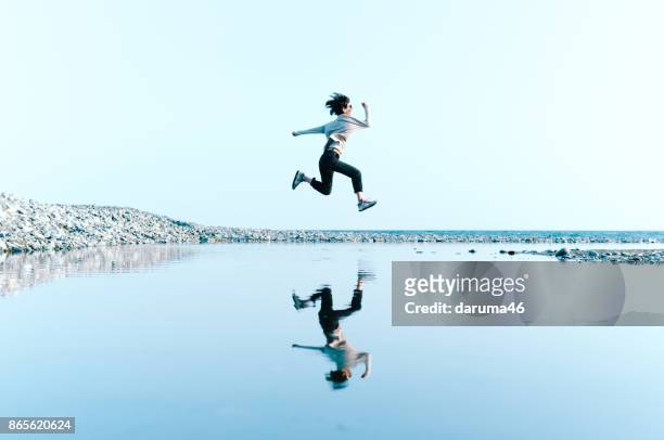 femme à sauter dans les airs au-dessus de l’eau disponibles dans une grande flaque - reflection photos et images de collection