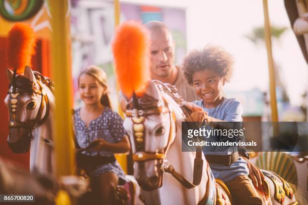 famiglia multietnica mista con padre che si diverte durante il carosello - carousel foto e immagini stock