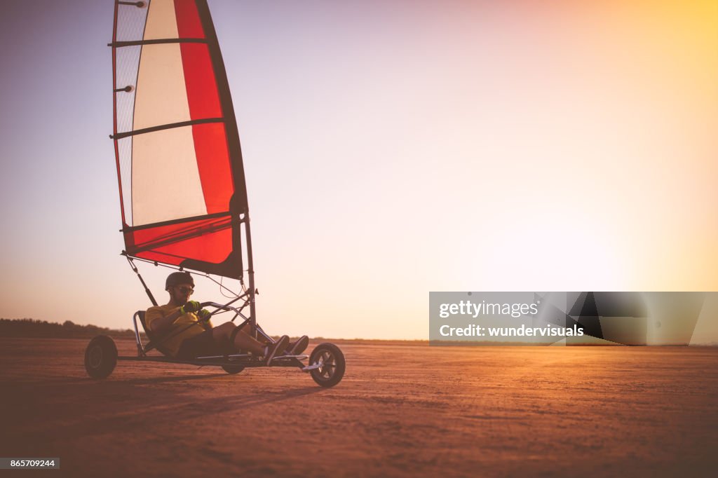Man van drijvende land zeilen blokart op het strand bij zonsondergang