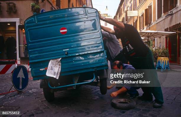 Team of men push over a small Ape van to change a flat tyre in a side street of the Italian capital, on 3rd November 1999, in Rome, Italy.