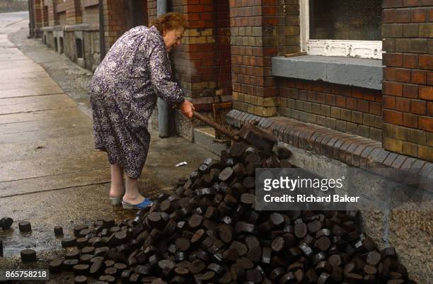 Six months after the fall of the Berlin Wall, a lady shovels East German Lignite coal briketts left outside her home, on 1st June 1990, in Aue,...