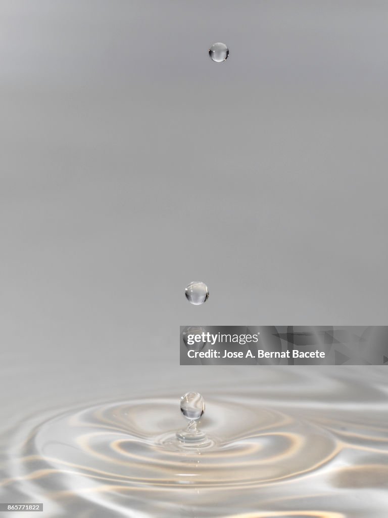 Group of drops on line suspended in the air, falling down on a water surface that forms figures and abstract forms, on a gray background
