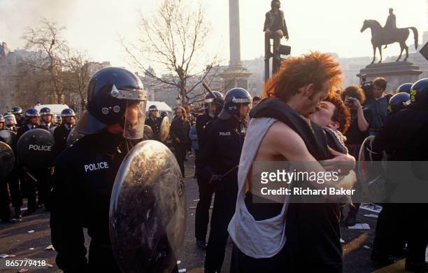 Couple kiss near police officers in the middle of the Poll Tax riot in the UK capital, on 31st March 1990, in Trafalgar Square, London, England....