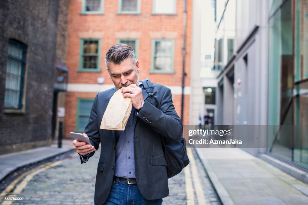 Businessman eating a sandwich and using smart phone