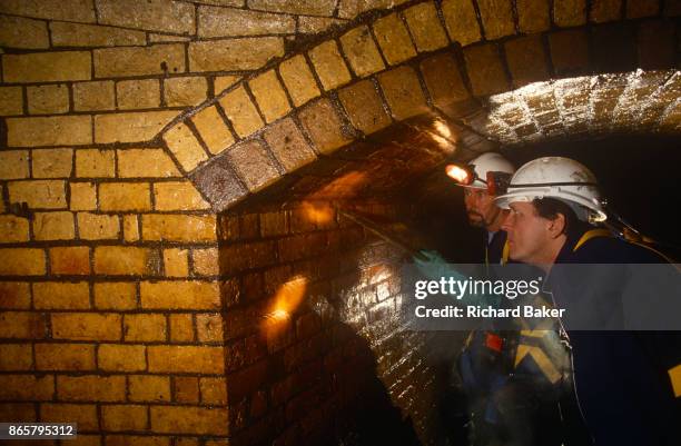 An inspection by the Thames Water Utilities sewer cleaning team looks closely at Victorian-era brick wall linings of the Fleet River's...