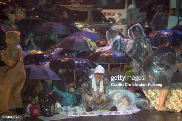 People take cover from torrential rain as they begin to queue and sleep on the streets overnight to attend Thailand's late King Bhumibol Adulyadej's...
