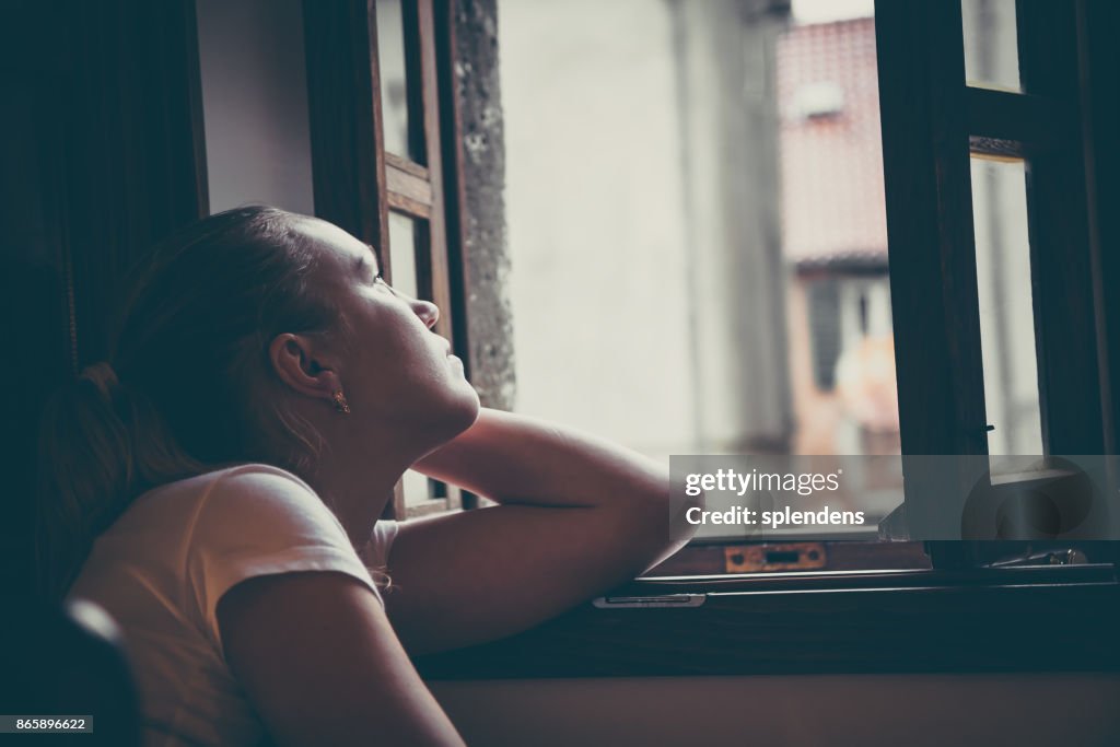 Lonely pensive women with thoughtful expression lost in thoughts thinking and looking in opened window in vintage style with dramatic mood